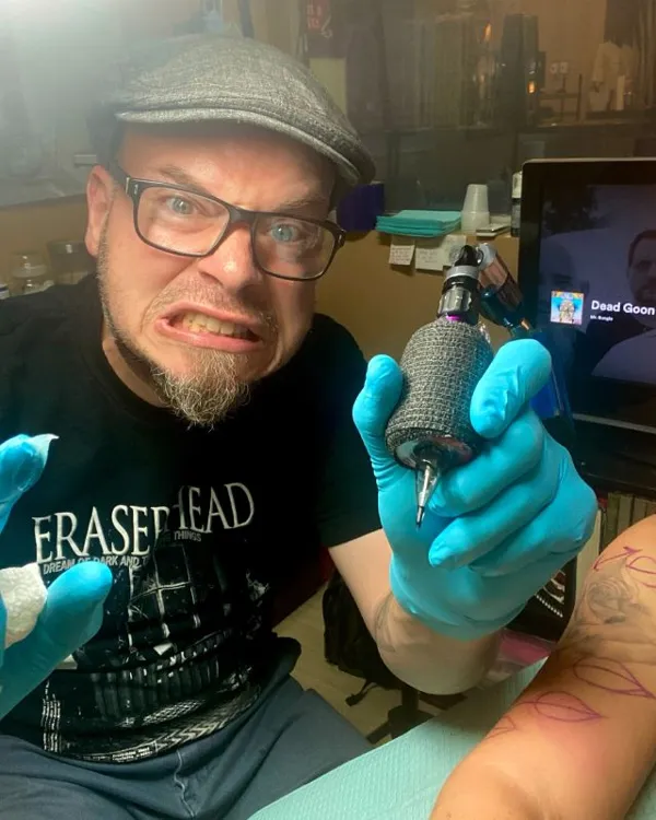 Tattoo artist Adrian Milan holding a tattoo machine, wearing blue gloves